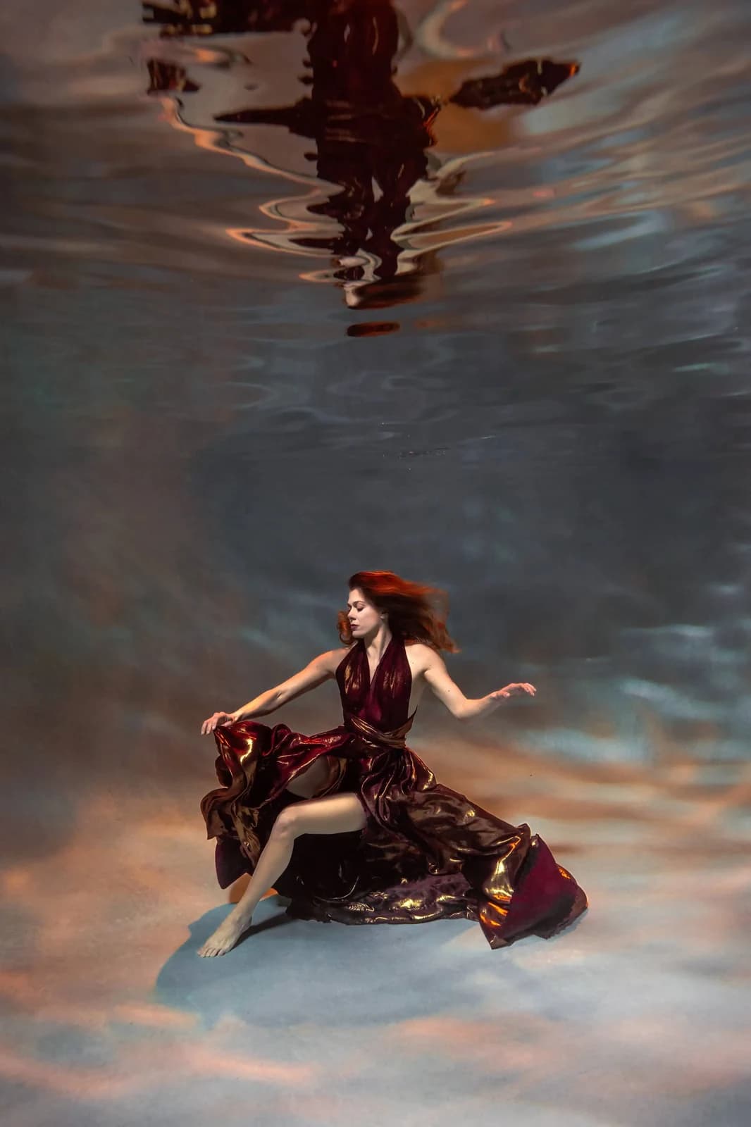 Woman floating underwater in a flowing burgundy dress — editorial underwater photography