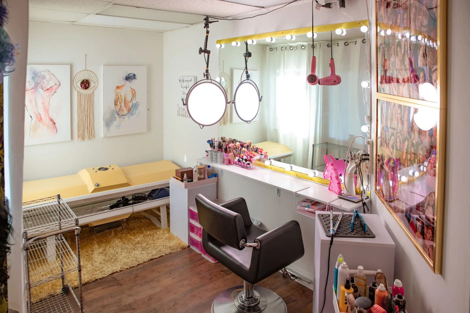 Casey Quist's studio hair and makeup station — salon chair, Hollywood vanity mirror, art prints on the wall, warm lighting