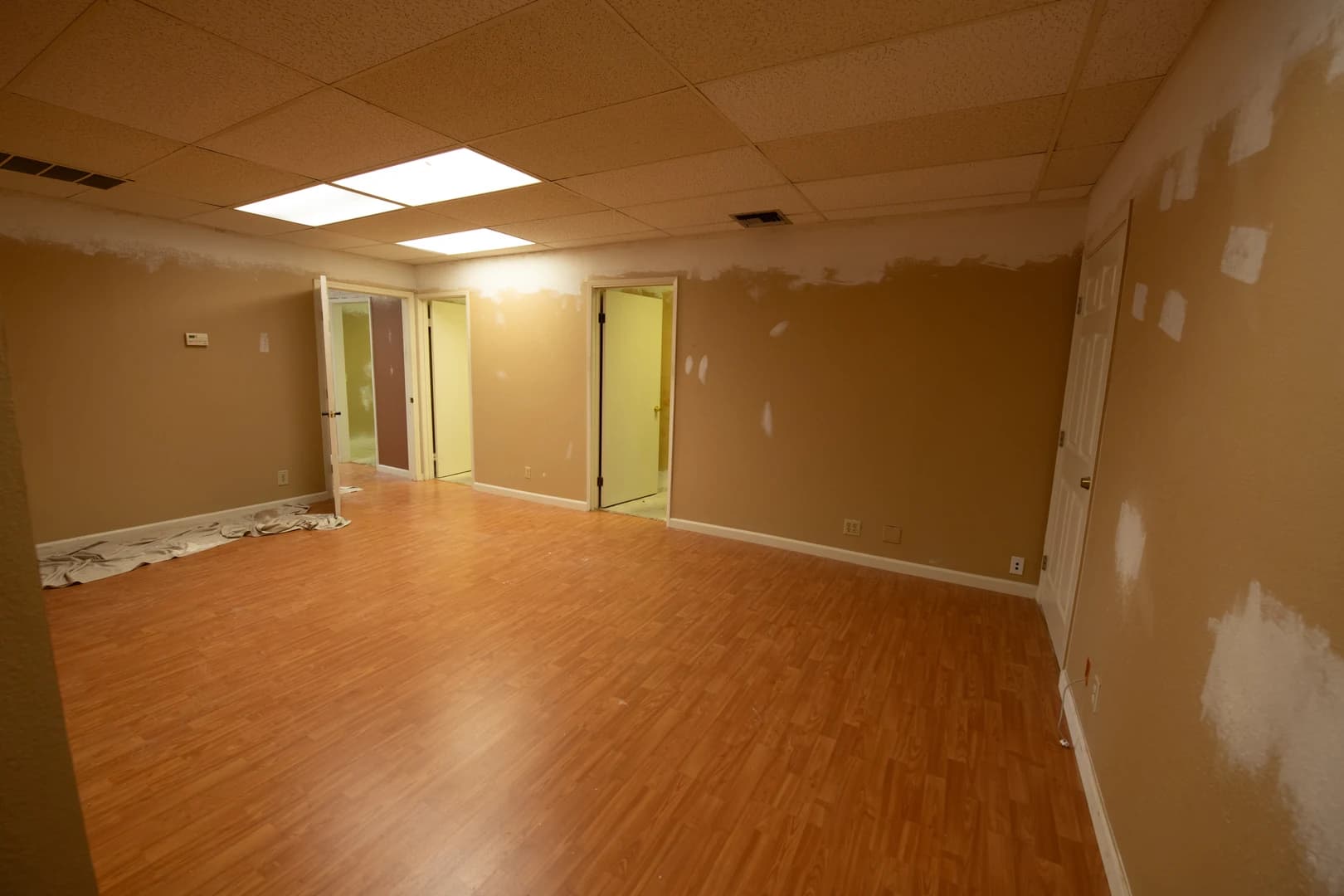 Mid-renovation interior of Casey Quist's Concord studio — laminate flooring laid, drywall compound being applied, drop ceiling in place
